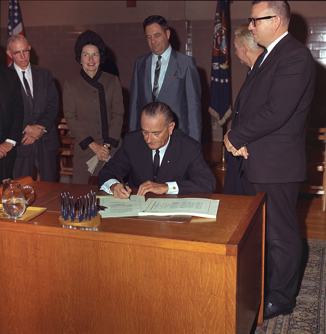 President Lyndon B. Johnson seated at a desk signing the Higher Education Act as officials look on